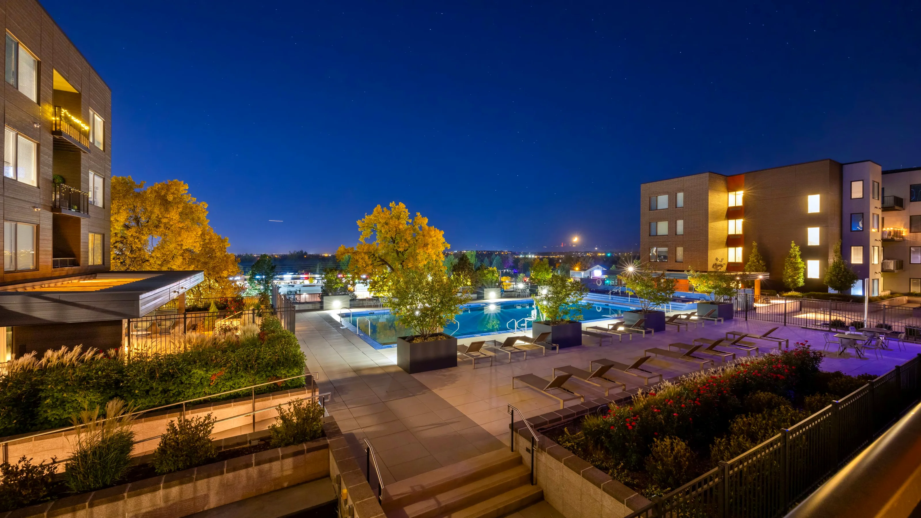 Complejo residencial al anochecer con la piscina iluminada y los jardines